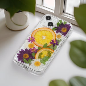 Elegantly designed clear phone case with a natural composition of pressed flowers and citrus, displayed on a bright windowsill, invoking a sense of tranquility.