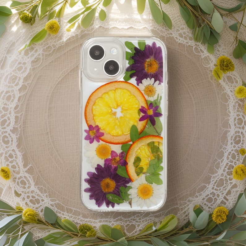 Elegant phone case with a lace background, adorned with a mix of pressed purple asters, sunny daisies, and vibrant orange slices, embodying a sophisticated blend of nature and vintage charm.
