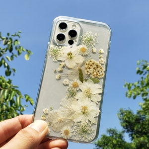 Transparent phone case with white pressed flowers held up to a clear blue sky, capturing the essence of SunnyPigStudio's delicate and natural design aesthetic.