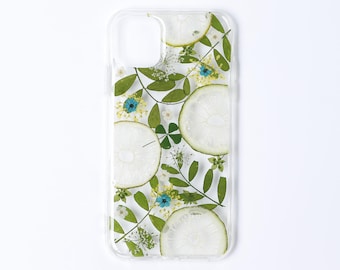 Könnte beinhalten: Eine transparente Handyhülle mit einem eingebetteten botanischen Design aus gepressten grünen Blättern, kleinen weißen Blüten, leuchtend blauen Blütenblättern und mehreren durchscheinenden, kreisförmigen Limettenscheiben auf der Rückseite.