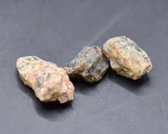May include: Three rough, green and brown gemstone crystals on a black background.