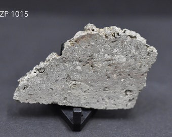 Può includere: Primo piano di una roccia grigia, dalla texture ruvida, di colore grigio chiaro. La roccia è su un supporto nero e il testo "ZP 1015" è visibile nell'angolo in alto a sinistra dell'immagine.