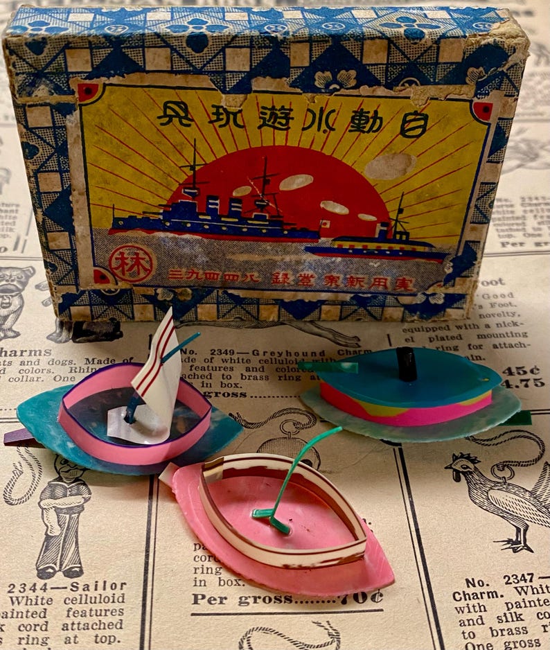 May include: Vintage toy boats in pink, blue, and teal with white sails and green masts. The boats are displayed with a box featuring a ship illustration and Japanese text. The box has a blue and yellow design.