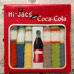 May include: Vintage Hi-Jacs for Coca-Cola box with colorful knitted cozies. The box is red with white text and a Coca-Cola bottle illustration. The cozies are in various colors, including blue, yellow, and green.