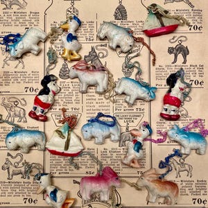 May include: A collection of miniature celluloid charms, including animals and figures, with painted details and attached cords. The charms are displayed on a vintage paper background with text and prices.