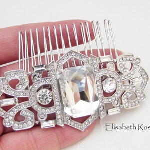 May include: Silver hair comb with a large clear rhinestone in the center and smaller rhinestones around the edges. The comb has a decorative design with a floral motif.