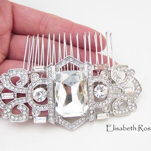 May include: Silver hair comb with a large clear crystal and smaller crystals around the edges. The comb has a decorative design with a repeating pattern.
