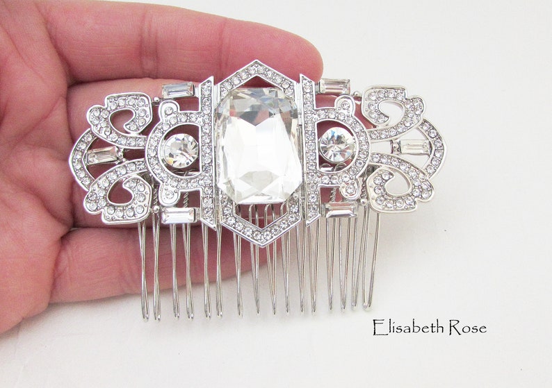 May include: Silver hair comb with a large clear crystal in the center and smaller crystals around the edges. The comb has a decorative design with a geometric pattern.