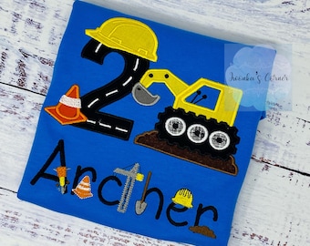 May include: A blue t-shirt with an embroidered design of a construction vehicle, the number 2, a construction hat, and a traffic cone. The text "Archer" is embroidered below the design.