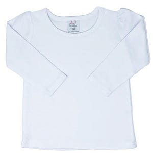 Puede incluir: Camiseta blanca de manga larga con cuello redondo y hombros abullonados. La camiseta tiene una peque&ntilde;a etiqueta con el texto "AJ Blanks 12M" en la parte delantera.