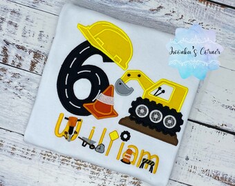 May include: A white t-shirt featuring a black number six, a yellow construction hat, a yellow construction vehicle, and the name "William" in yellow lettering. The shirt is adorned with construction-themed embellishments, including a traffic cone, a wrench, and a stop sign.