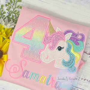May include: Pink t-shirt with a rainbow glitter number 4 and a unicorn with a rainbow mane. The name "Samara" is embroidered in rainbow colors below the unicorn.