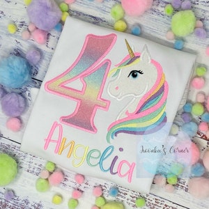 May include: White t-shirt with a colorful embroidered unicorn and the number 4. The number 4 and the name "Angelica" are in a rainbow gradient. The unicorn has a gold horn and a rainbow mane.
