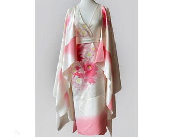 Può includere: Un kimono bianco con un motivo floreale rosa e bianco. Il kimono ha un collo a V e maniche lunghe. Le maniche sono legate ai polsi. Il kimono è fatto di seta.