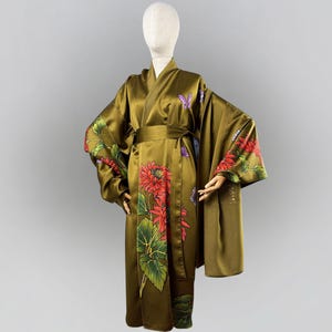 Puede incluir: Kimono verde oliva con diseños florales y de mariposas. El kimono presenta grandes flores rojas con hojas verdes y mariposas moradas. Las mangas y los paneles frontales están adornados con el estampado floral. Un cinturón a juego ciñe la cintura.