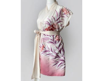Può includere: Accappatoio di seta color crema con un design floreale. L'accappatoio presenta un'ampia cintura e una sciarpa fluente. Il motivo floreale include fiori e foglie rosa e viola, con una sfumatura dal crema al rosa sull'orlo.