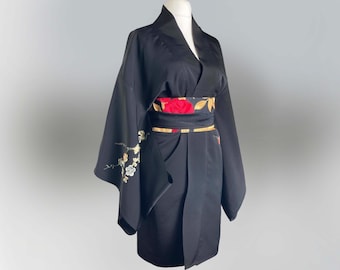 May include: A black kimono with a floral obi belt. The kimono has long sleeves and a V-neck. The obi belt is decorated with red and gold flowers.