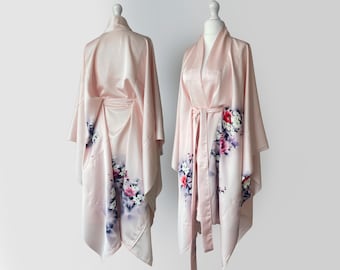 May include: A pale pink satin robe with a floral print in shades of pink, purple, and white. The robe has long sleeves and a tie belt.