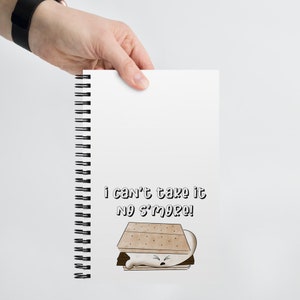 May include: A white spiral notebook with a brown and white illustration of a s'more with a grumpy face. The text "i can't take it no s'more!" is printed below the illustration.