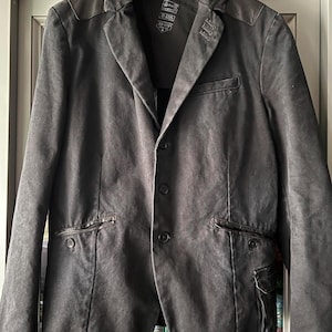 May include: A black blazer with a single-breasted closure, two flap pockets, and a zippered pocket on the right side. The blazer has a leather collar and shoulder patches. The label on the blazer reads "G-Star RAW" and "Size: S/M - 170/78".