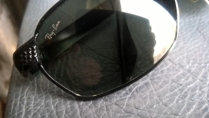 May include: Black Ray-Ban sunglasses with a textured frame and dark lenses.