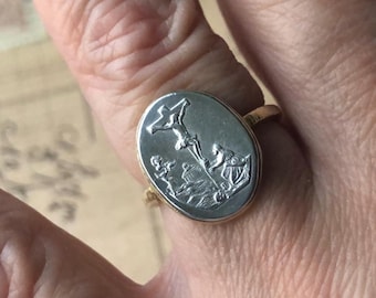 May include: A gold ring with a silver oval-shaped setting featuring a raised image of a person on a cross with two other figures standing nearby.