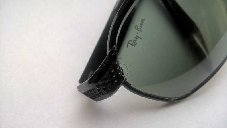 May include: Black Ray-Ban sunglasses with green lenses. The sunglasses have a textured design on the arms.