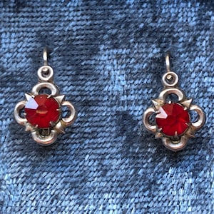 Może przedstawiać: Para srebrnych kolczyków z czerwonymi kamieniami szlachetnymi. Kolczyki mają wzór koniczyny.