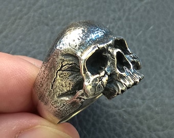 Può includere: Un anello in argento a forma di teschio con un design dettagliato. Il teschio è di profilo e ha una superficie testurizzata.