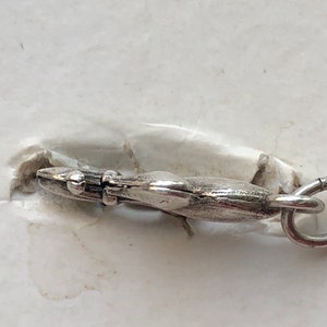 May include: Silver charm with a detailed design, featuring a loop for attaching to a bracelet or necklace.