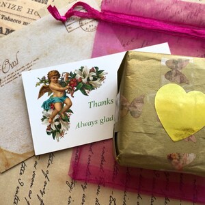 May include: A small, gold-wrapped package with a gold heart sticker and a thank you note with an angel illustration. The note says "Thanks Always glad".