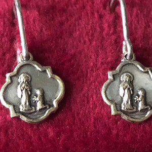 May include: A pair of silver earrings with a gold-toned image of a woman and a child. The image is set in a silver frame with a scalloped edge.