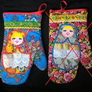 May include: Two blue and red oven mitts with a Russian doll design. The doll is embroidered with a white lace trim and has a yellow face with red lips. The mitts are numbered #1 and #2.