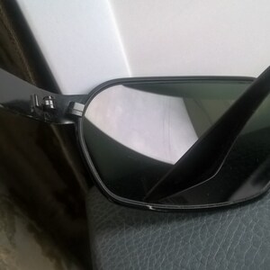 May include: Black sunglasses with a dark green lens and a gold accent on the side. The sunglasses are made of plastic and have a classic aviator style.