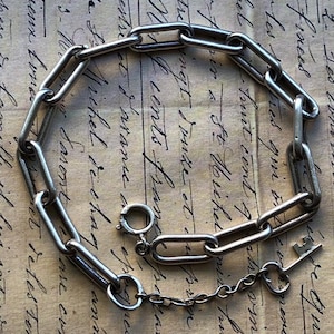 May include: A silver-toned chain bracelet with elongated links and a small key charm. The bracelet is displayed on a vintage paper background with handwritten script.
