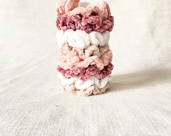 May include: A stack of five scrunchies in shades of pink and white. The scrunchies are made of a soft, fuzzy material and have a ruffled texture.