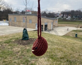 May include: A brown crocheted pouch with a smiling face, hanging from a brown cord.