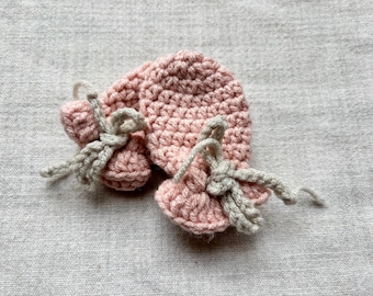 May include: A pair of pink crocheted baby booties with beige crocheted bows.