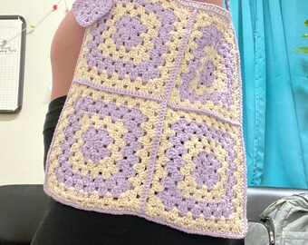 May include: A crocheted shoulder bag made of lavender and cream yarn. The bag is made of four granny squares.