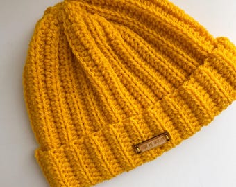 May include: A yellow crocheted beanie with a brown leather tag that says "Mary Me Crochet".