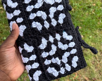 May include: Black and white crocheted bag with a drawstring closure. The bag is made of a thick yarn and has a geometric pattern.