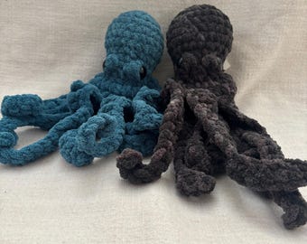 May include: Two handmade crochet octopus plushies. One is teal, the other is dark gray. The plushies have round heads, small black eyes, and eight curled tentacles. The soft, textured yarn gives them a cuddly appearance.