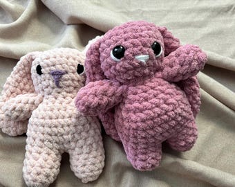 May include: Two crocheted bunny plushies, one in pink and one in a darker shade of pink. Both bunnies have black eyes and a white nose.