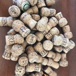 Puede incluir: Una colección de tapones de botella de corcho con varios nombres de marca y logotipos, incluyendo "CAVA", "FRE", "GRM6", "ENE", "PENDA" y "www.jw".