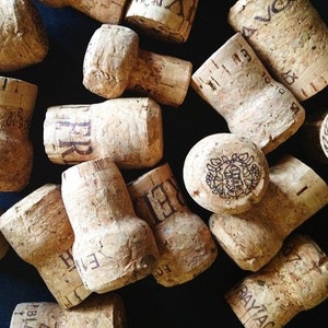 May include: A close-up of a pile of cork bottle stoppers. The stoppers are made of natural cork and have a variety of shapes and sizes. Some of the stoppers have writing on them, including the words "BRUT" and "CAVA".