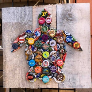 May include: A colorful turtle mosaic made from bottle caps on a wooden background. The turtle is made from a variety of different colored bottle caps, including red, blue, green, yellow, and orange. The bottle caps are arranged in a pattern that resembles a turtle's shell.