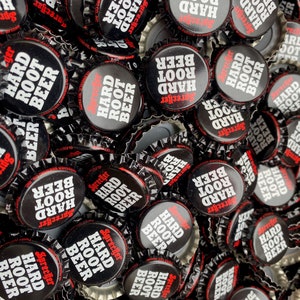 May include: A close-up of a pile of black bottle caps with white text that reads "Sprecher Hard Root Beer".