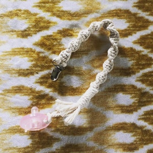 May include: A white cotton rope pacifier clip with a silver clip and a pink pacifier.