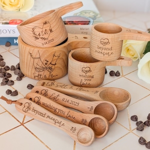 May include: A collection of wooden measuring cups and spoons with engraved designs and text. The cups and spoons are light brown and feature heart and floral motifs, along with phrases like "wishing you love" and "beyond measure."