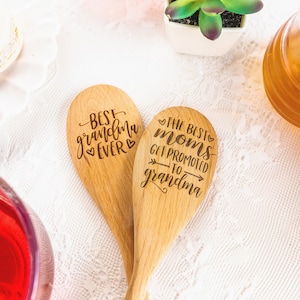 May include: Two light-colored wooden spoons with dark laser-engraved text. One spoon reads "BEST grandma EVER" with heart icons. The other spoon reads "THE BEST moms GET PROMOTED TO grandma" with arrow and heart accents.